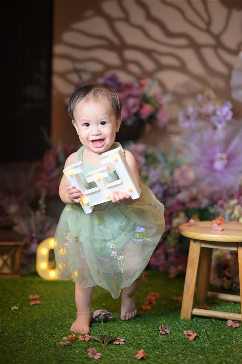Tanya smiling and standing with a light-up letter beside a wooden stool